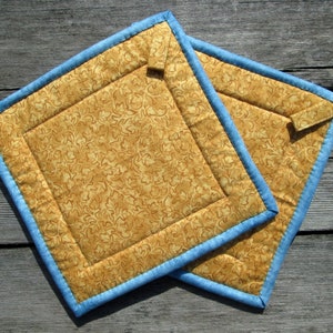 May include: Two quilted pot holders with a blue trim and a brown floral pattern.