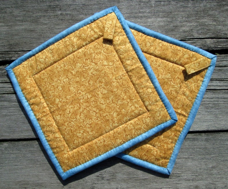 May include: Two quilted pot holders with a blue trim and a brown floral pattern.