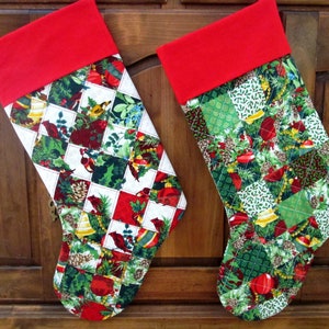May include: Two red and white Christmas stockings with a quilted patchwork design featuring a variety of holiday motifs, including pine cones, holly, bells, and birds.