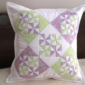 May include: A white pillow with a green and pink geometric pattern. The pattern is made up of triangles and squares. The pillow is quilted and has a white border.