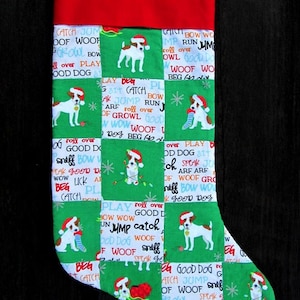 May include: A green and red Christmas stocking with a patchwork design featuring a dog wearing a Santa hat and the words "Catch Jump, Good Dog, Woof, Sniff, Play, Roll Over, Beg, Speak, Arf, Growl, Bow Wow".
