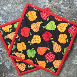 May include: Two black quilted pot holders with a red border. The pot holders feature a repeating pattern of pears and apples in various colors and designs.