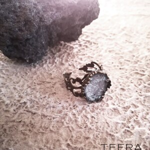 May include: A silver ring with a white, sparkly, oval-shaped stone set in a filigree design.