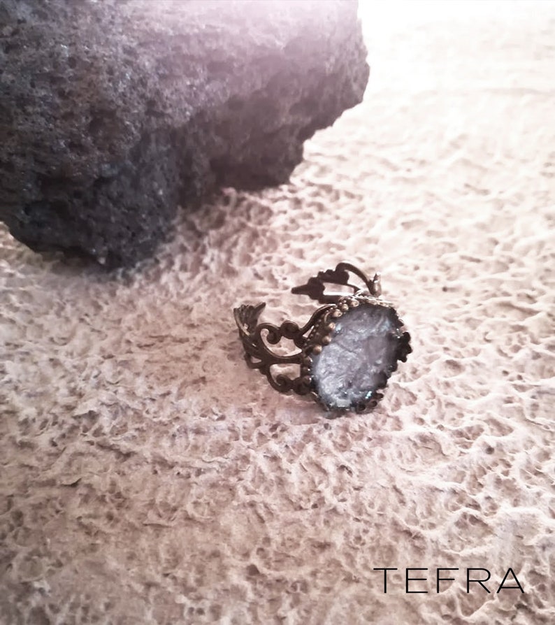 May include: A silver ring with a white, sparkly, oval-shaped stone set in a filigree design.
