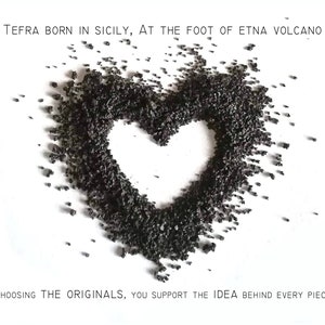 May include: A heart shape made of black volcanic rock from Mount Etna in Sicily. The text "TEFRA BORN IN SICILY, AT THE FOOT OF ETNA VOLCANO" is at the top of the image. The text "CHOOSING THE ORIGINALS, YOU SUPPORT THE IDEA BEHIND EVERY PIECE" is at the bottom of the image.