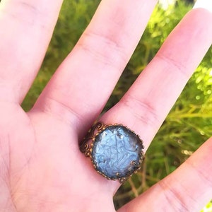 May include: A silver and white ring with a detailed, ornate, bronze setting. The ring is on a finger.