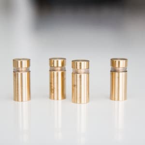 May include: Four gold-colored metal shelf supports with clear plastic inserts. The supports are arranged in a row on a white surface.