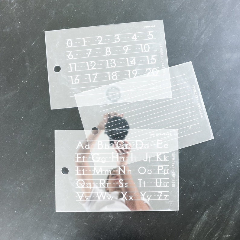 May include: Two clear plastic stencils with white numbers and letters. The top stencil has numbers 0-20. The bottom stencil has the alphabet.