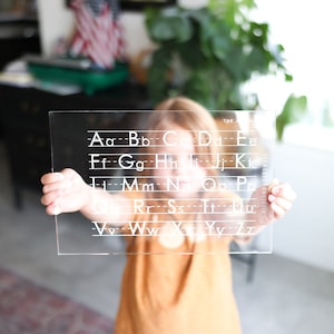 May include: A clear plastic alphabet chart with white lettering. The chart has lines for tracing letters. The text on the chart reads "The Alphabet" and "Highland Hardware".