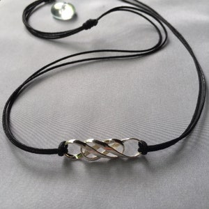 May include: A silver infinity symbol pendant necklace on a black cord.