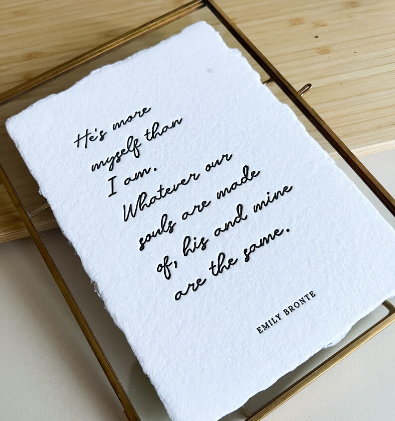 May include: A white framed print with a black handwritten quote by Emily Bront&euml; that reads: "He's more myself than I am. Whatever our souls are made of, his and mine are the same."
