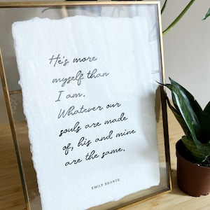May include: A framed print with a white background and black text. The text reads: "He's more myself than I am. Whatever our souls are made of, his and mine are the same." The text is signed "Emily Bronte".