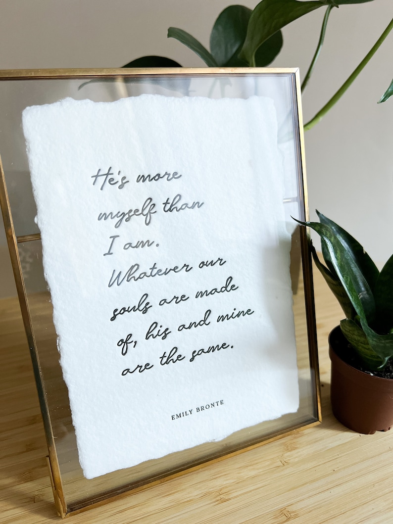 May include: A framed print with a white background and black text. The text reads: "He's more myself than I am. Whatever our souls are made of, his and mine are the same." The text is signed "Emily Bronte".