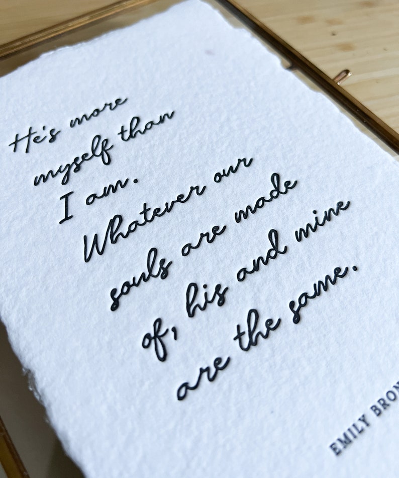 May include: A white paper print with black ink calligraphy that reads "He's more myself than I am. Whatever our souls are made of, his and mine are the same." The text is signed "EMILY BRON".