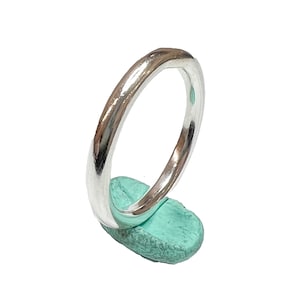 May include: A simple silver band ring, shown on a turquoise green surface.