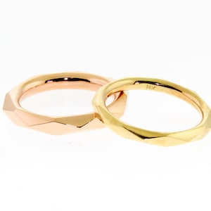 May include: Two gold wedding bands with a faceted design. The band on the left is rose gold and the band on the right is yellow gold. The yellow gold band is marked "14K".