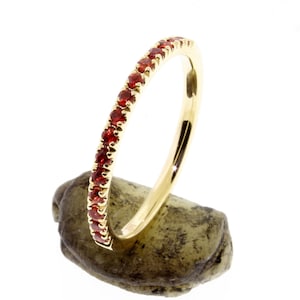 May include: A gold band ring with a row of small red gemstones.