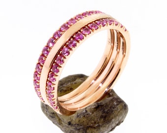 May include: A rose gold band ring with three rows of pink sapphires set in the metal. The ring is on a rough, brown rock.