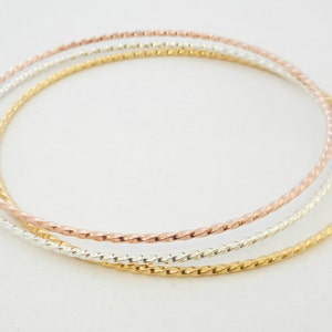 Puede incluir: Tres pulseras de oro, plata y oro rosa con un diseño de cuerda trenzada.