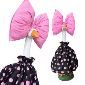 May include: A white goose statue wearing a large pink fabric bow on its head and a black skirt featuring a repeating pattern of small pink pumpkins. The goose has an orange beak and is standing on a green base, shown in two different views.
