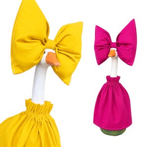 May include: Two white goose figurines, each wearing a fabric outfit. One goose wears a bright yellow dress with a matching oversized bow on its head. The other goose wears a vibrant fuchsia dress with a matching oversized bow on its head.