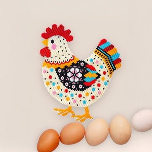 Peut inclure: Une figurine de poulet en perles colorées sur un fond blanc avec six œufs blancs devant elle.