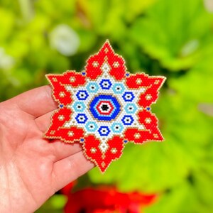 Puede incluir: Una estrella roja, blanca y azul de cuentas con un diseño de ojo central. La estrella está hecha de cuentas pequeñas y tiene un contorno dorado.