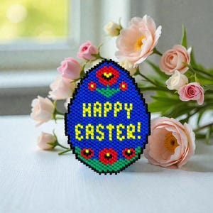Peut inclure: Décoration en forme d'œuf bleu avec l'inscription jaune "HAPPY EASTER!". Le motif comprend des accents de fleurs rouges et une bordure verte. La décoration est placée devant un bouquet de roses roses.