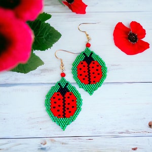 May include: A pair of green and red ladybug earrings with gold hooks. The earrings are made of beads and are shaped like ladybugs with black spots.