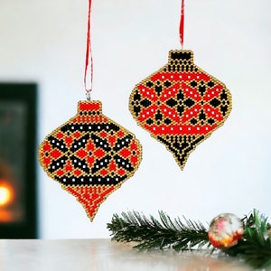 May include: Two red, black and gold beaded Christmas ornaments hanging from red string. The ornaments are shaped like teardrops and have a geometric pattern.