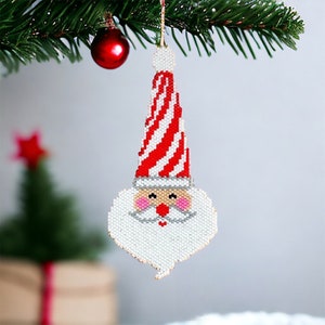May include: A beaded Christmas ornament shaped like Santa Claus's face. The ornament is white with a red and white striped hat. Santa has a white beard, pink cheeks, and a red nose.