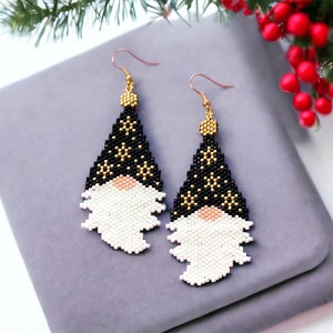 May include: A pair of beaded earrings featuring a gnome design. The gnomes are wearing black hats with gold stars and have white beards. The earrings are hanging from a gray surface.