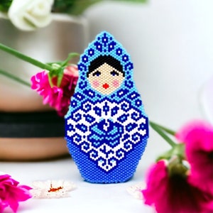 May include: A blue and white beaded Russian nesting doll, or matryoshka doll, with a traditional folk art design. The doll is made of beads and has a blue and white floral pattern.