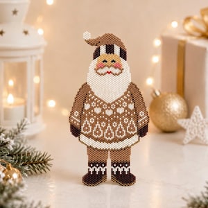 May include: A beaded Santa Claus Christmas ornament. The ornament features a brown and white colour scheme with a detailed design. The Santa has a white beard, a brown hat, and a patterned sweater. The ornament is standing on a white surface.