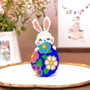 May include: A white beaded bunny peeking out of a blue and multi-colored beaded Easter egg.