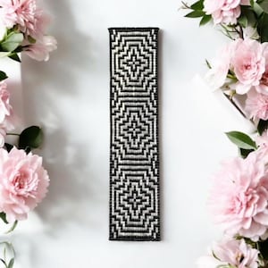 May include: A black and white beaded bookmark with a geometric pattern. The bookmark is about 10 inches long and 1 inch wide.