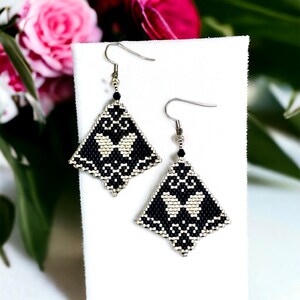 May include: A pair of black and silver beaded earrings with a geometric diamond shape and a floral pattern. The earrings have a silver hook closure.
