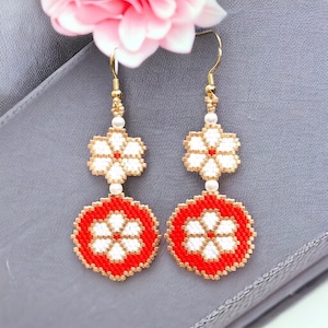 May include: A pair of dangle earrings with red and white flower designs. The earrings are made of beads and have a gold-colored metal finding.