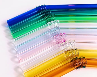 May include: A set of colorful glass drinking straws with a spiral design at the top. The straws are arranged in a rainbow pattern, with blue, green, light blue, pink, clear, yellow, and orange straws.