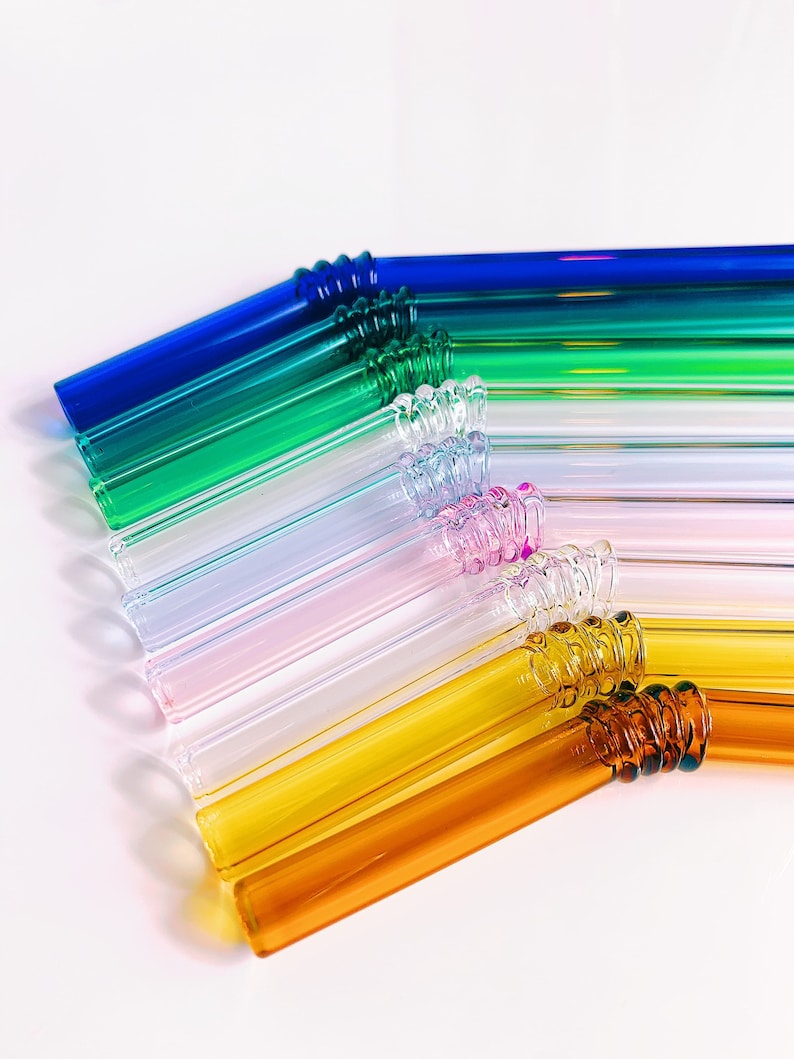 Puede incluir: Un juego de pajitas para beber de vidrio de colores con un dise&ntilde;o en espiral en la parte superior. Las pajitas est&aacute;n dispuestas en forma de arco&iacute;ris, con pajitas azules, verdes, azul claro, rosas, transparentes, amarillas y naranjas.