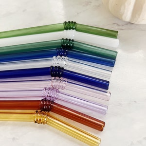 Puede incluir: Un juego de ocho pajitas para beber de vidrio en varios colores, incluyendo verde, azul, morado, marr&oacute;n y amarillo. Las pajitas est&aacute;n dobladas y tienen un dise&ntilde;o texturizado en la curva.