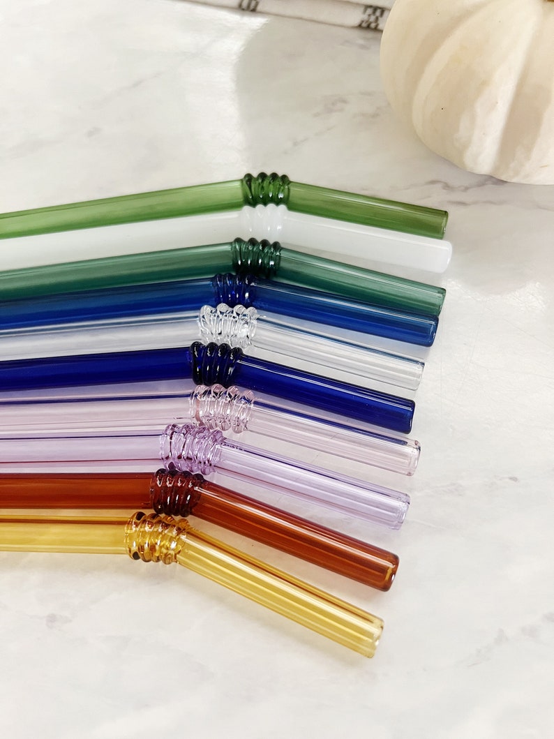 Puede incluir: Un juego de ocho pajitas para beber de vidrio en varios colores, incluyendo verde, azul, morado, marr&oacute;n y amarillo. Las pajitas est&aacute;n dobladas y tienen un dise&ntilde;o texturizado en la curva.