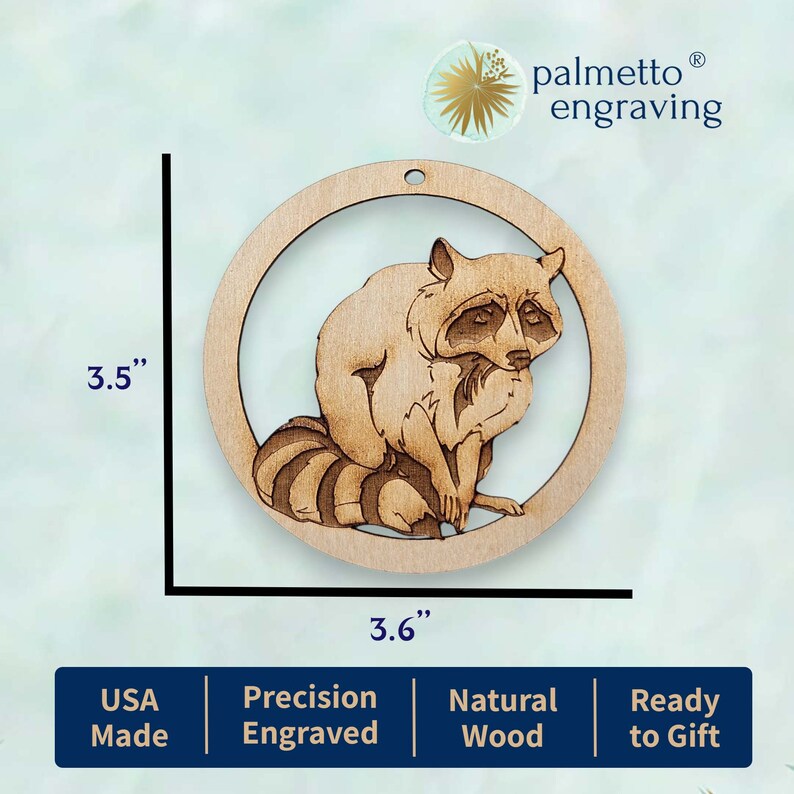 May include: A 3.5 inch round wooden ornament featuring a laser-cut design of a raccoon. The ornament is made of natural wood and is ready to gift. The ornament is engraved with the text "palmetto&reg; engraving".