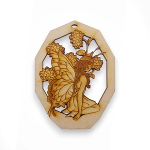 May include: A wooden cutout of a fairy with wings, sitting with flowers in her hair. The fairy is surrounded by a decorative frame.