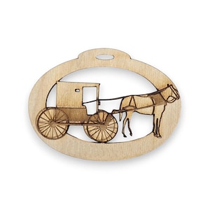 May include: A wooden ornament shaped like an oval with a cutout of a horse-drawn buggy. The ornament is a light brown color and has a hole at the top for hanging.