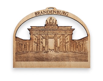 May include: A wooden ornament shaped like an archway with a laser-etched image of the Brandenburg Gate in Berlin, Germany. The ornament is labeled "BRANDENBURG" at the top.