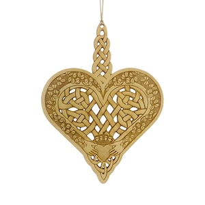 May include: A light brown wooden heart-shaped ornament featuring an intricate openwork Celtic knot pattern. The design includes a border of carved shamrocks and a central Claddagh motif showing two hands holding a crowned heart, suspended by a cord.