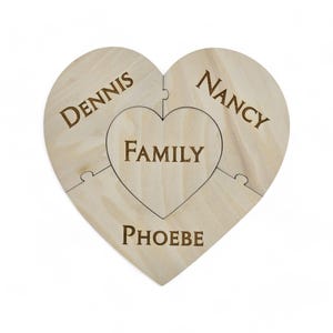 May include: A wooden heart-shaped puzzle with four pieces. The center piece says "FAMILY" and the other three pieces say "DENNIS", "NANCY", and "PHOEBE".