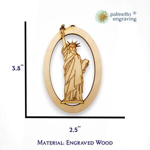 May include: A wooden ornament featuring a detailed engraving of the Statue of Liberty. The ornament is 3.8 inches tall and 2.5 inches wide. It is made of engraved wood.