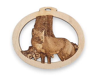 May include: A wooden ornament featuring a detailed laser-cut design of a fox standing in front of a tree trunk. The ornament is circular and has a hole at the top for hanging.